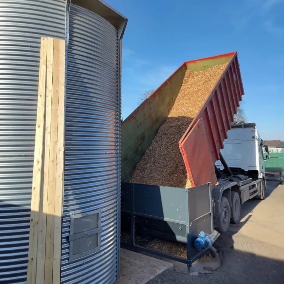 Déversement de plaquettes bois dans l'auge qui les soufflera dans le silo